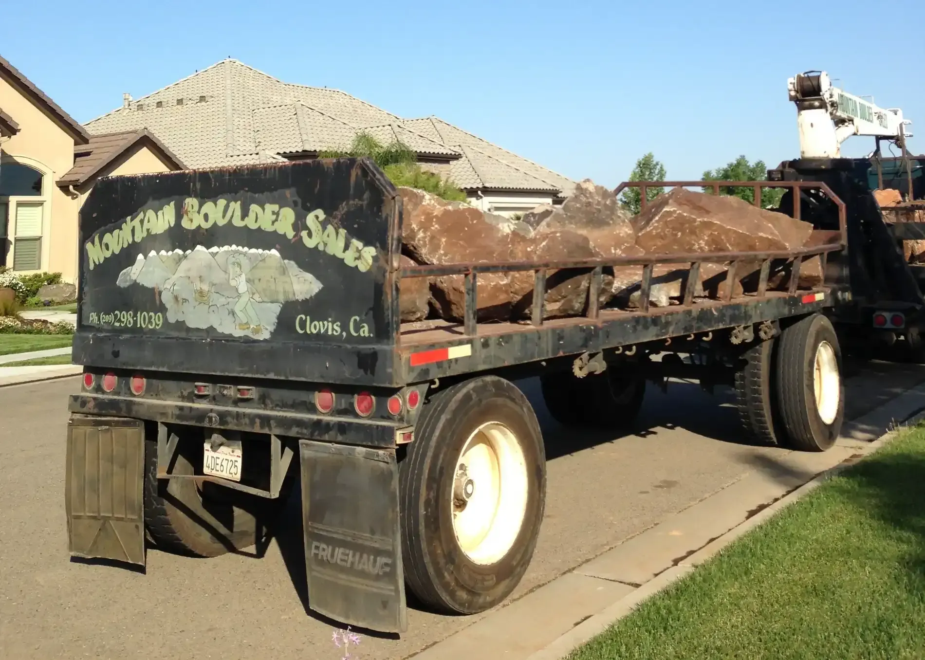 Truck loaded with soil or mulch parked on a suburban street beside a house and lawn