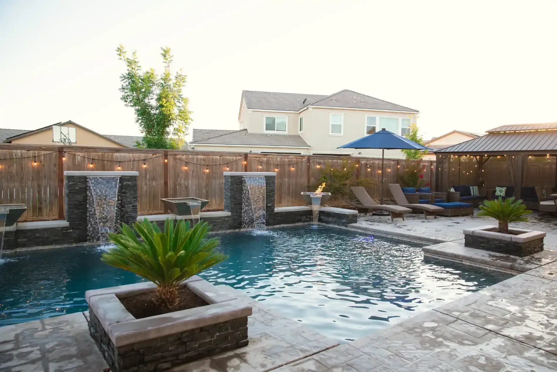 Backyard pool with stone deck, waterfall walls, and lounge chairs under bright daylight