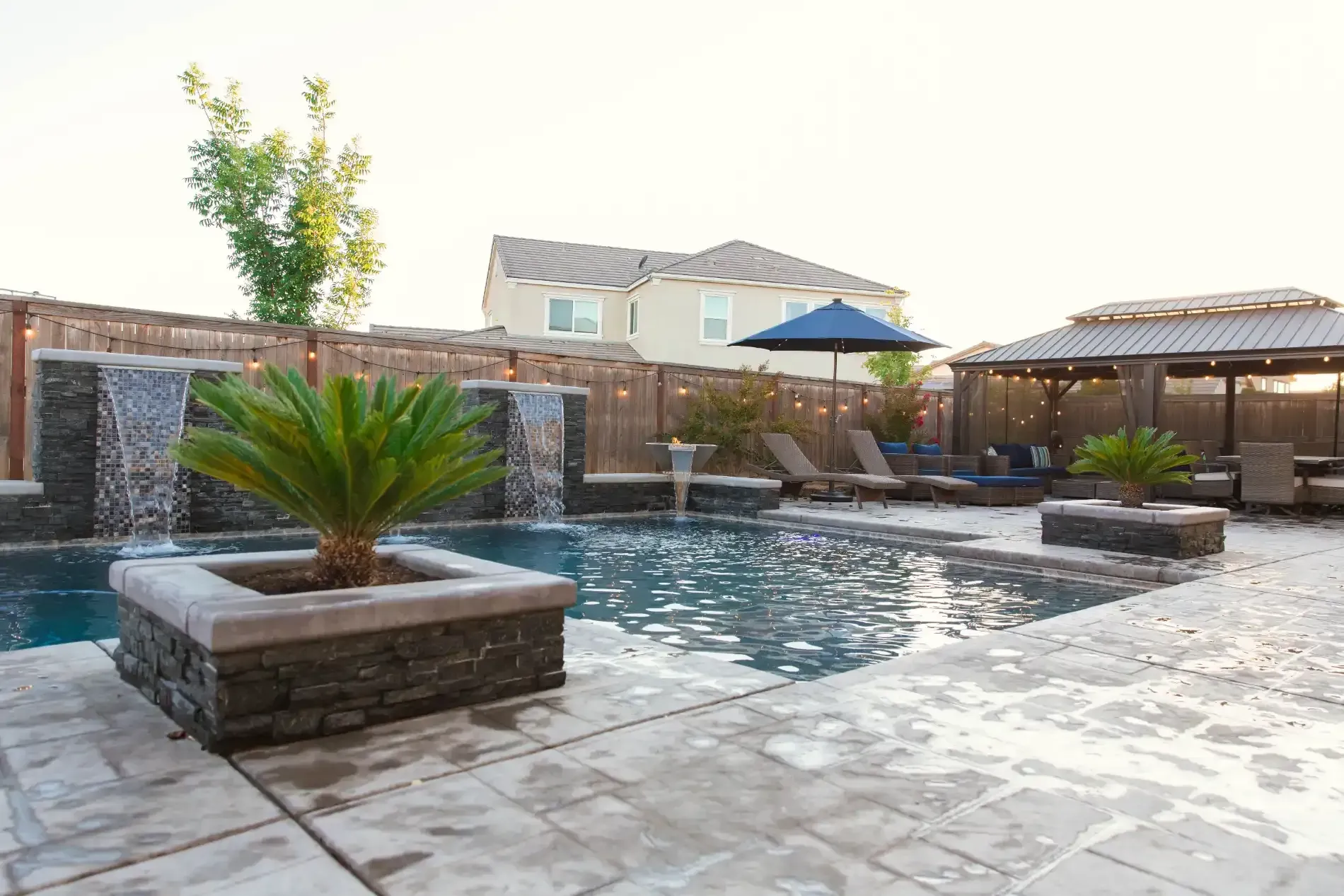 Modern backyard with a swimming pool, stone patio, planters, and pergola seating area.