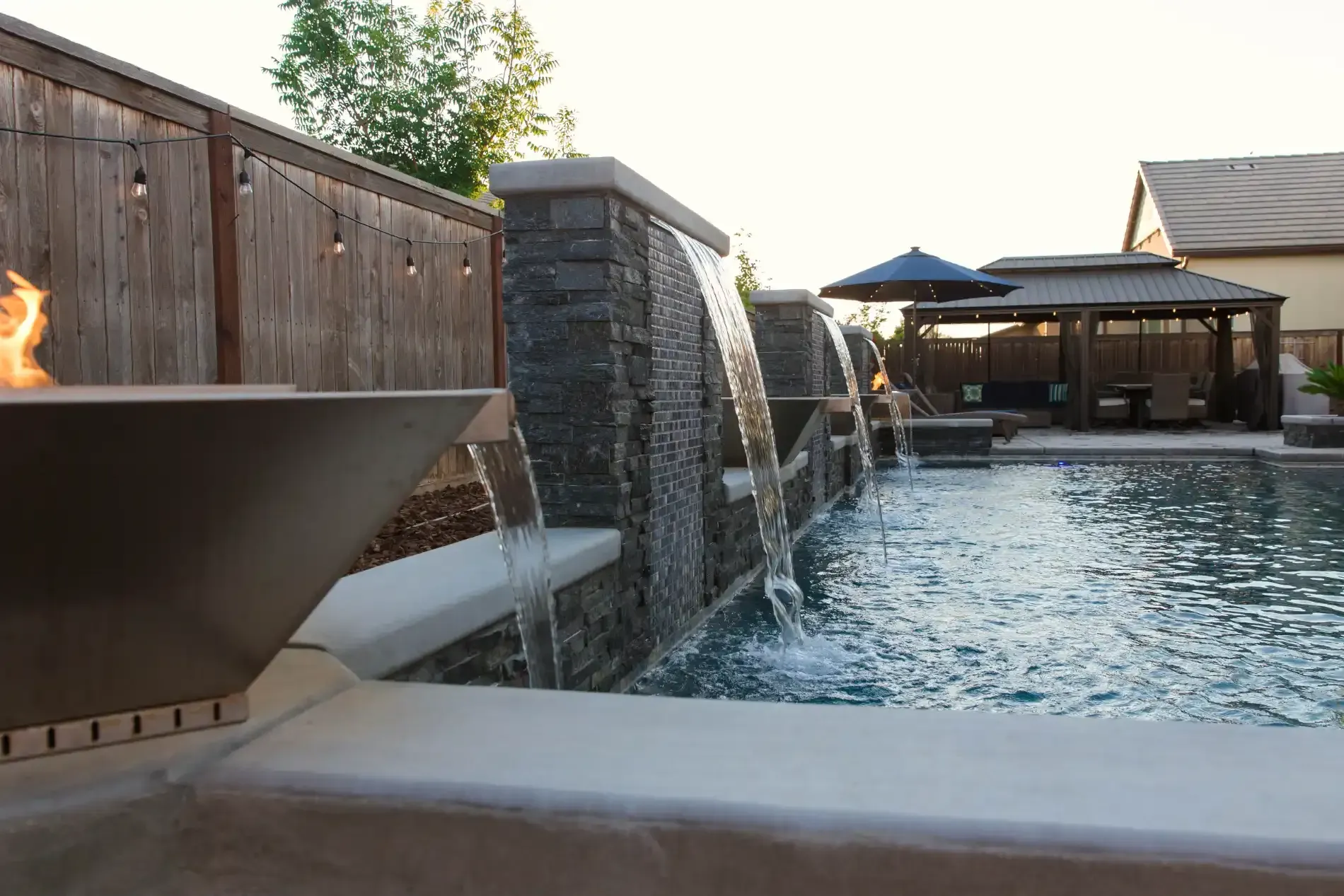 Outdoor pool with a stone waterfall, fire feature, and cabana at sunset