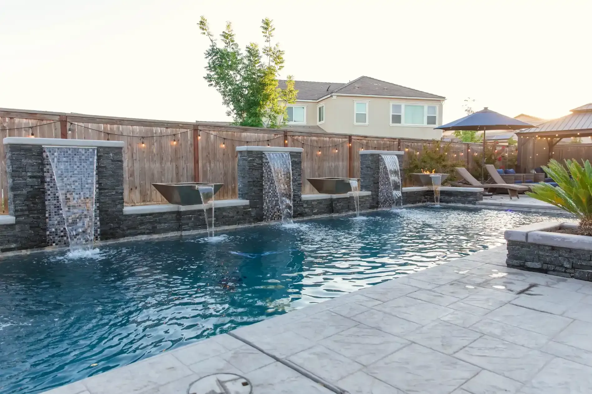 Backyard pool with stone water features and patio at sunset