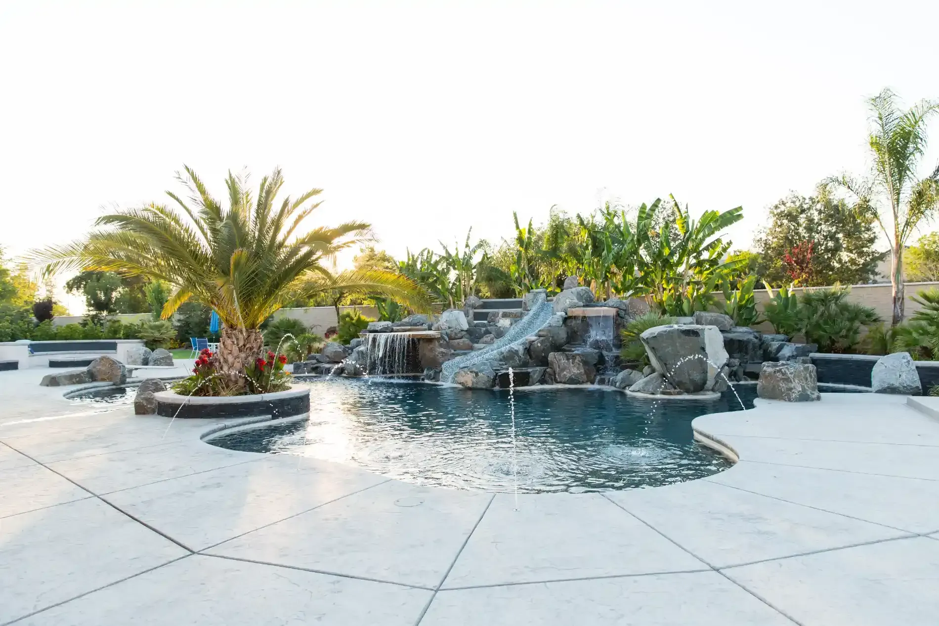 Luxury backyard pool with waterfall, palm trees, and stone landscaping at sunset