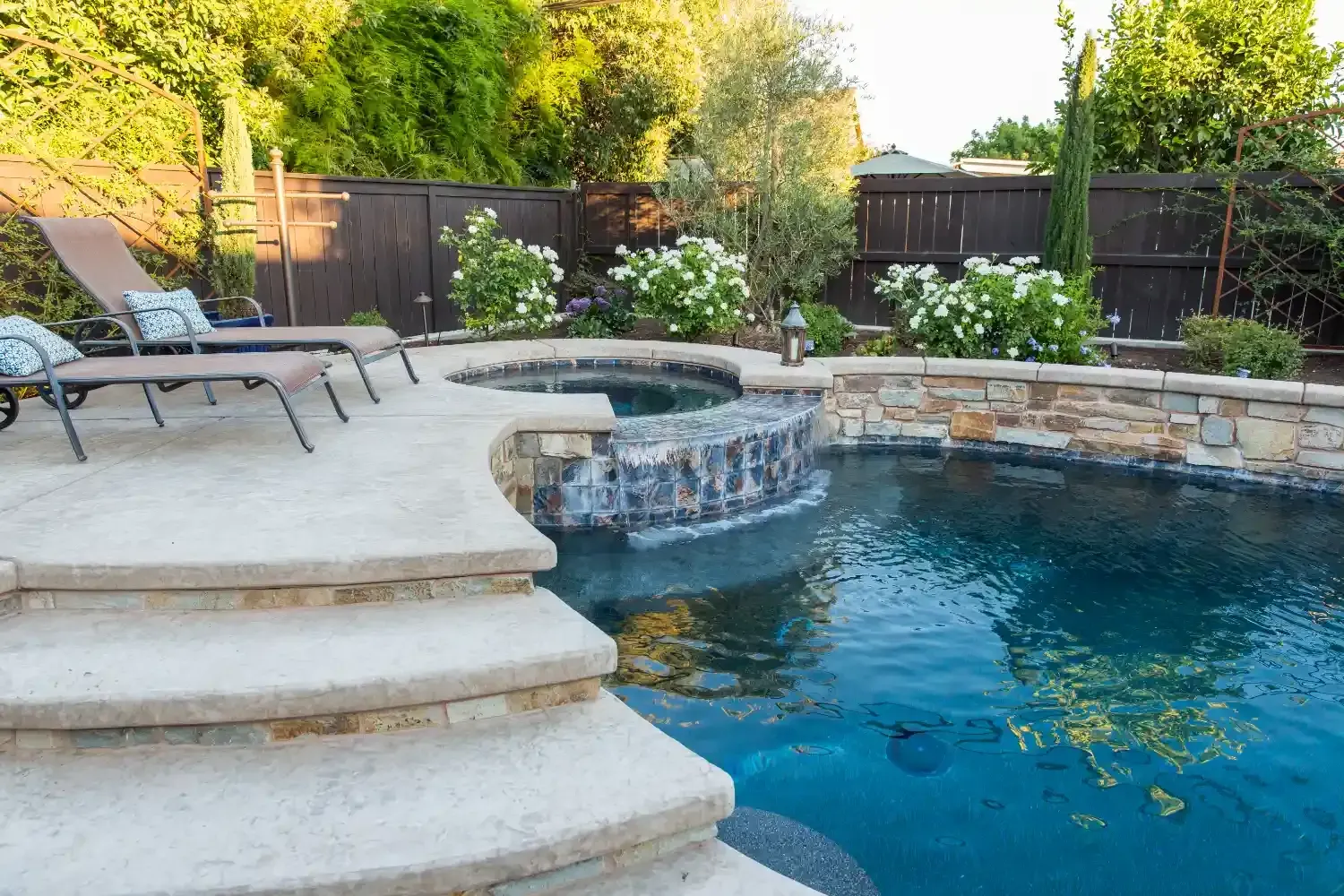 Backyard pool with stone steps, waterfall feature, lounge chairs, and lush greenery