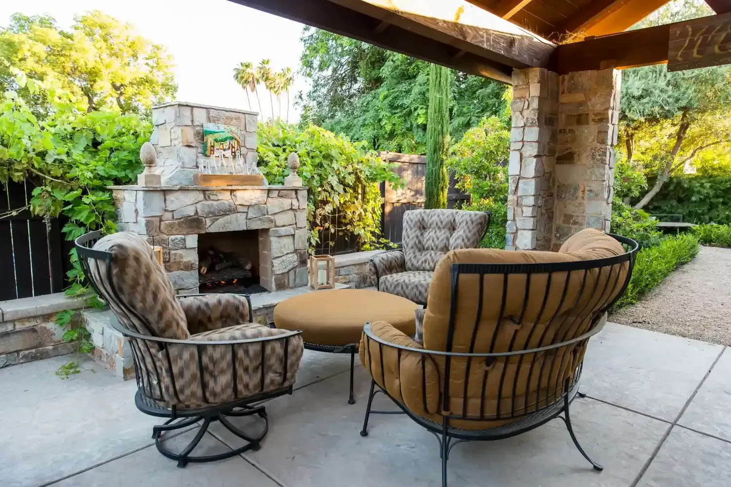 Covered patio with wicker seating around a stone fireplace in a landscaped backyard