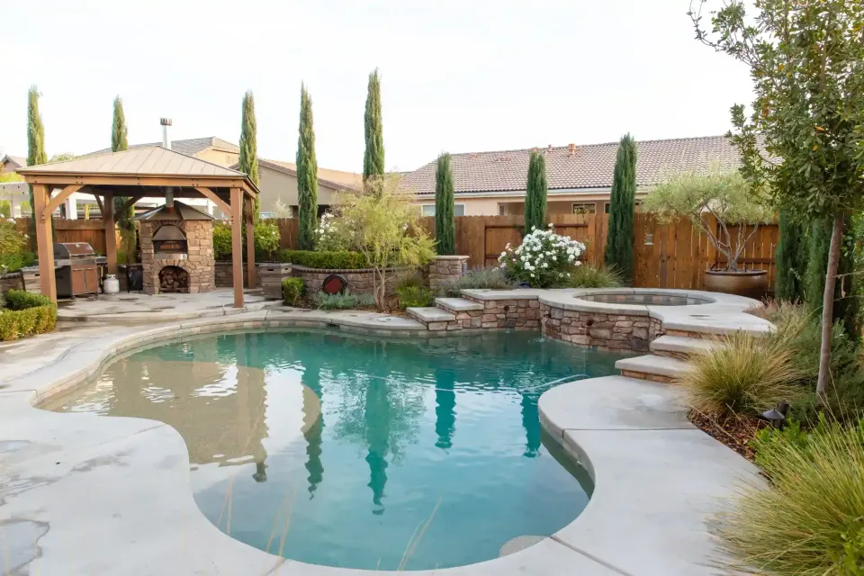 Backyard pool with stone deck, gazebo, and desert landscaping under a cloudy sky