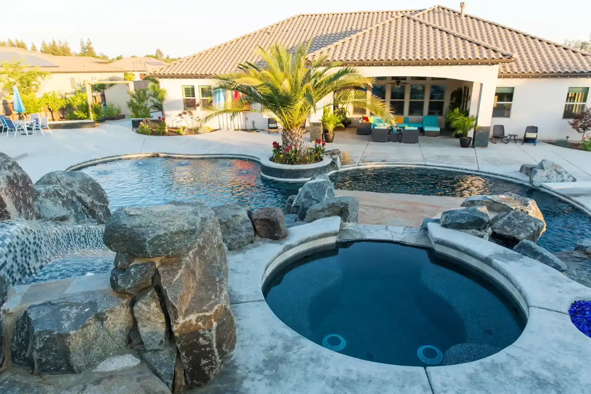 Luxury backyard pool with rock waterfall, circular spa, and palm trees beside a house