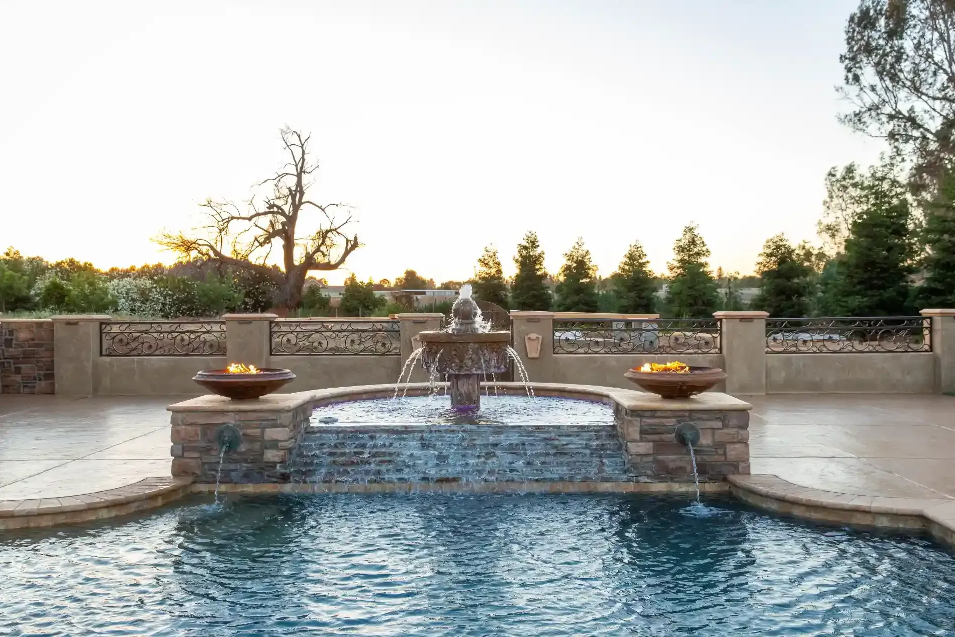 Backyard pool with stone waterfall and fire bowls at sunset