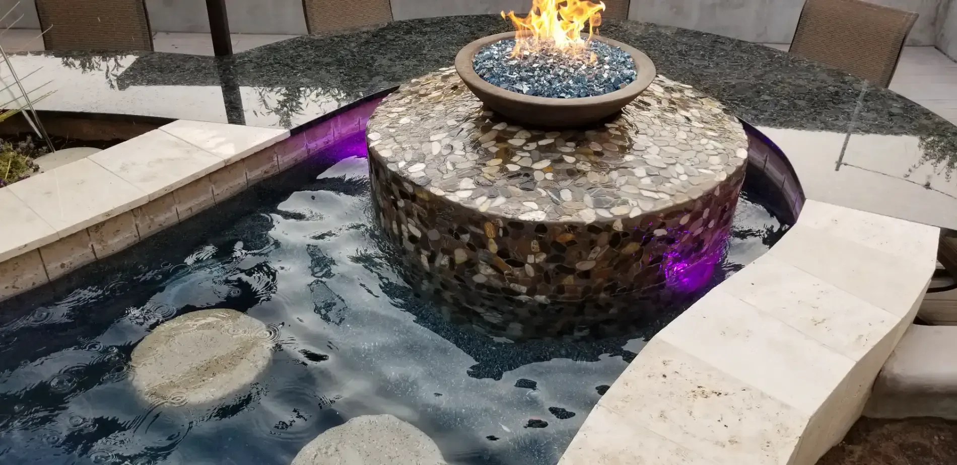 Outdoor fire bowl on a raised stone fountain in a curved tiled water feature