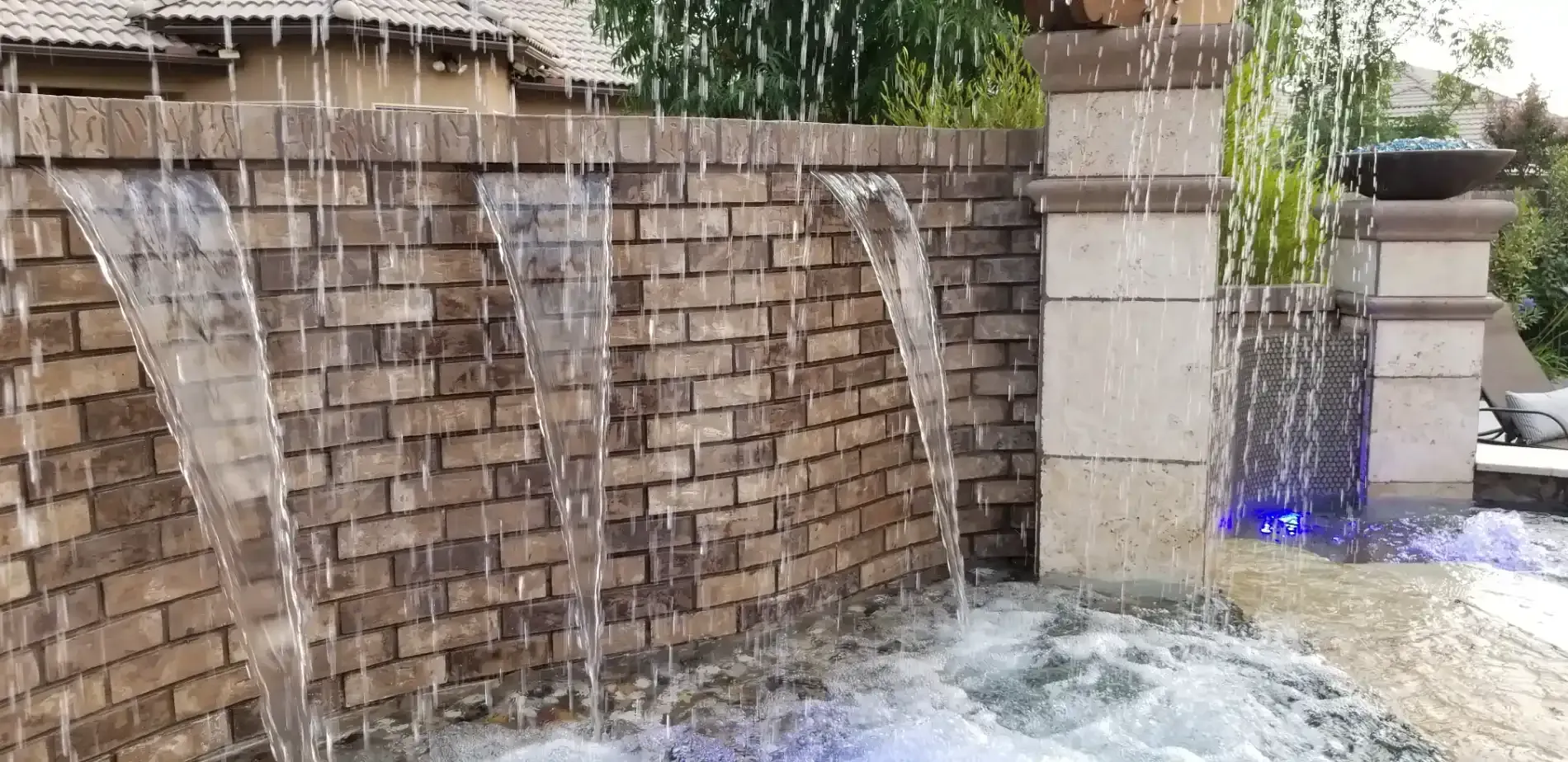 Water cascading over a brick wall into a foamy pool, with a small blue light on the right