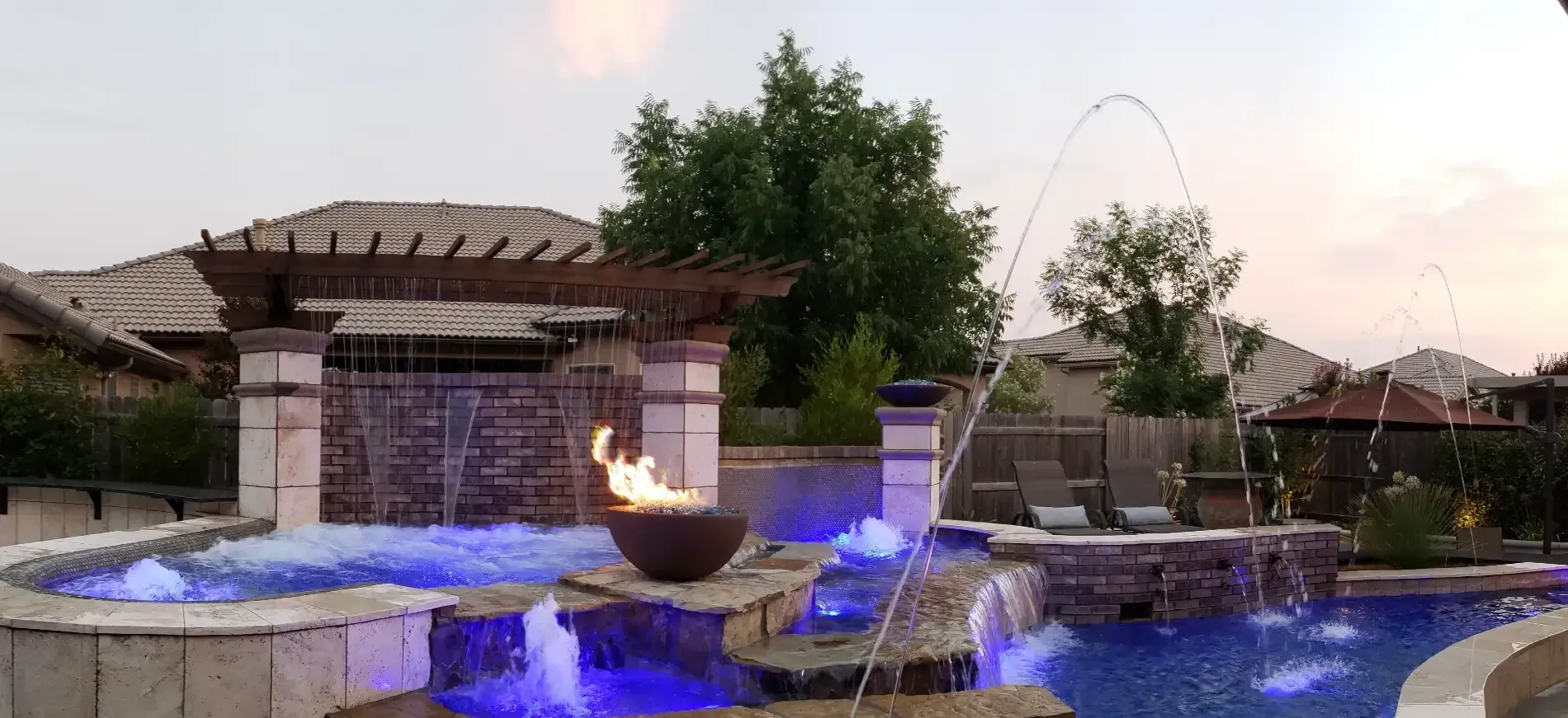 Backyard stone fountain with glowing blue lights at dusk, water cascading into a pool