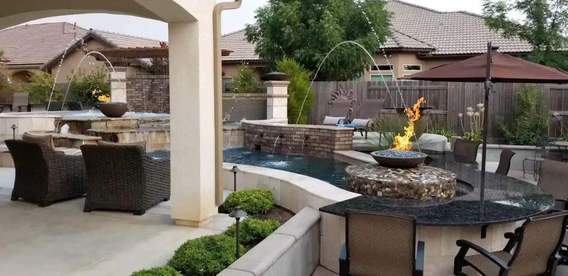 Backyard patio with wicker seating, fire pit, stone wall, and pool under a covered pergola