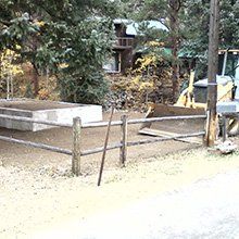 Wooden fence with a backhoe and building in the background. Gravel and dirt ground.