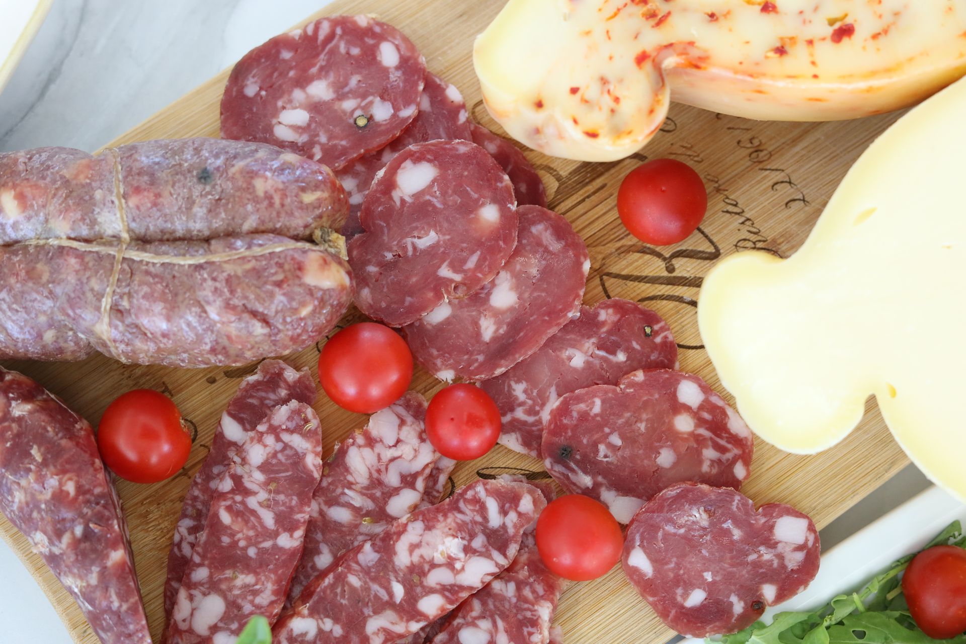 Un tagliere di salumi con salame affettato, pomodorini e formaggio.