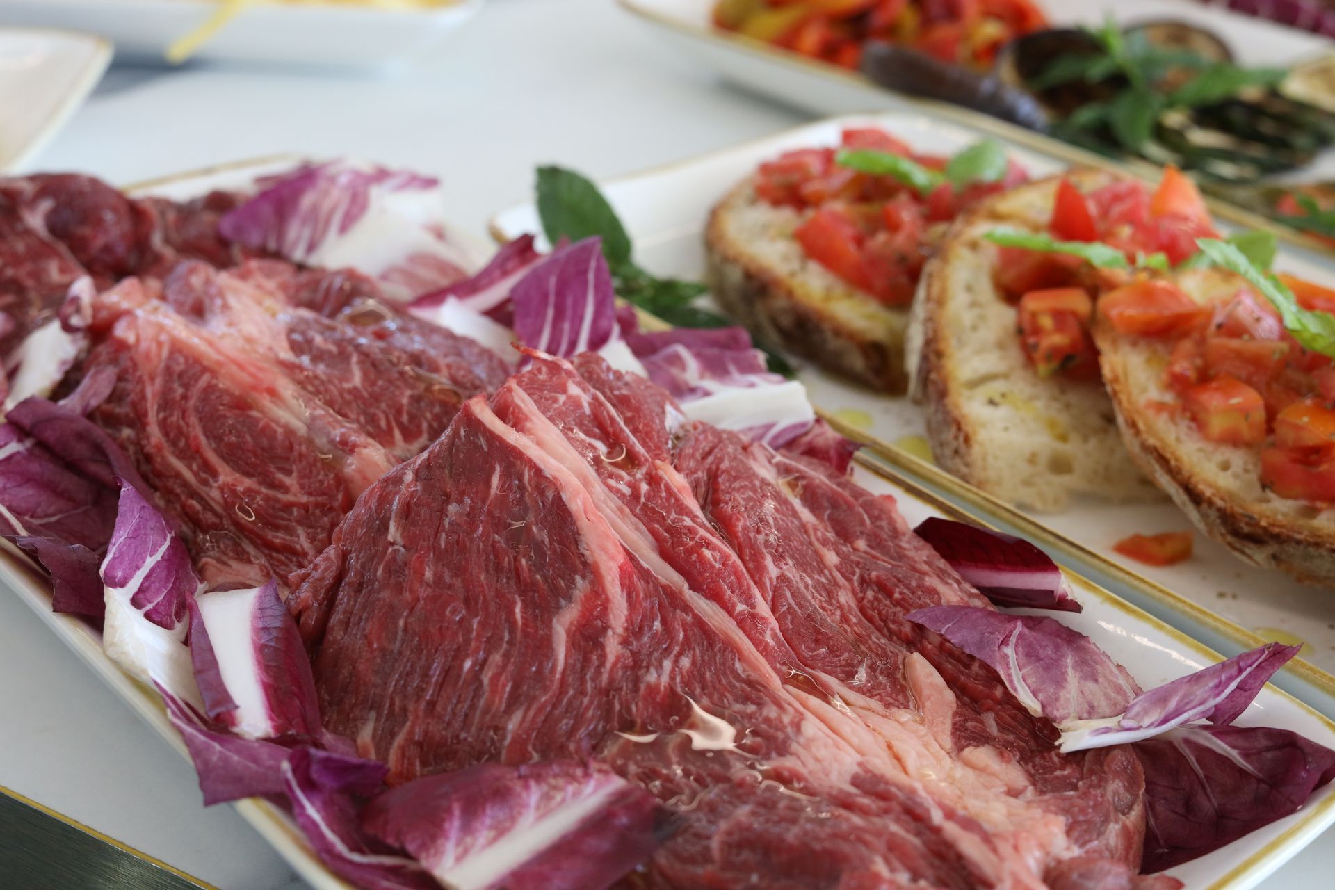 Primo piano di un piatto con carne cruda tagliata a fettine sottili, radicchio rosso e pane tostato condito con pomodori.