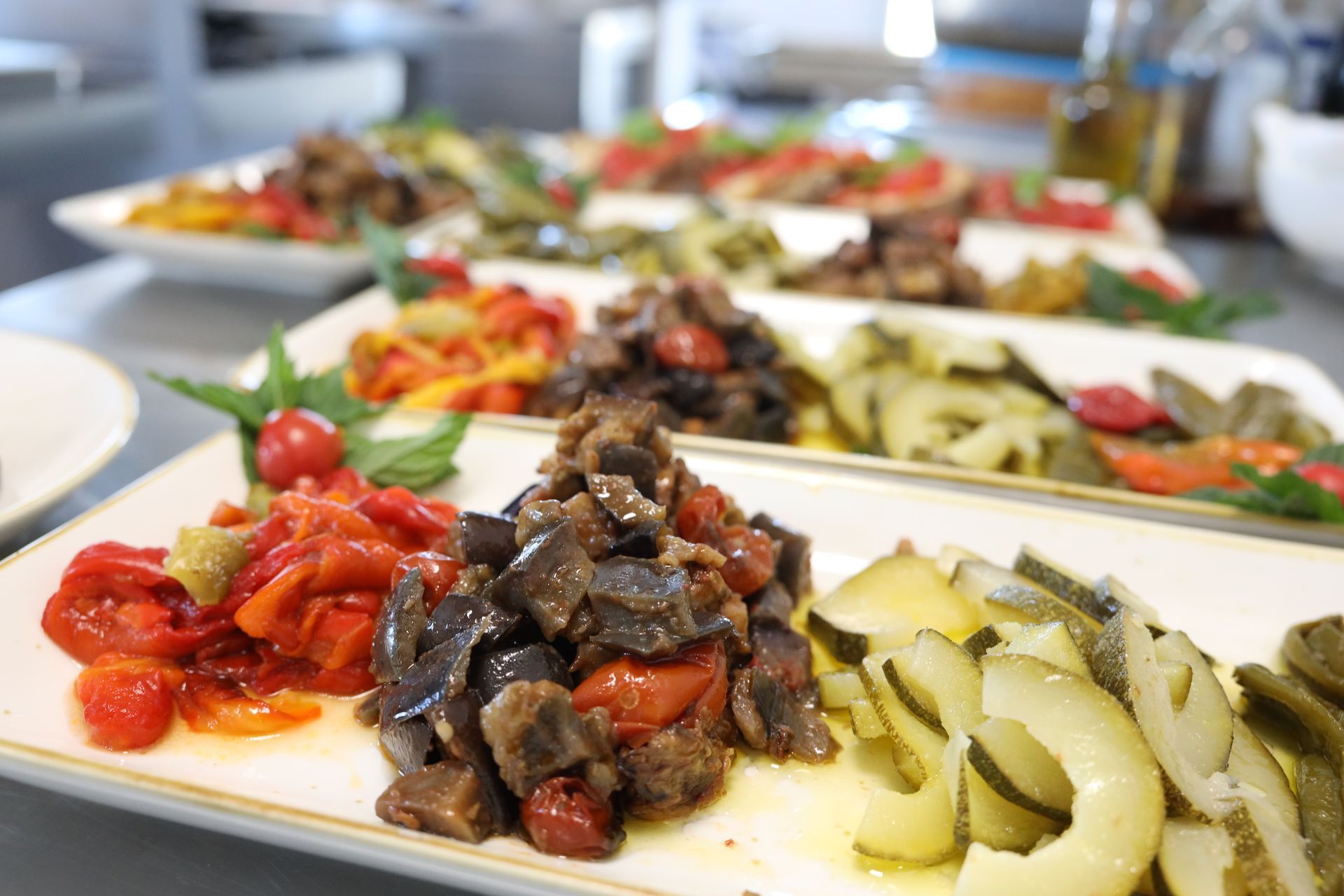 Vassoi di verdure colorate assortite, tra cui peperoni arrostiti, melanzane e zucchine, disposti su una superficie da cucina.