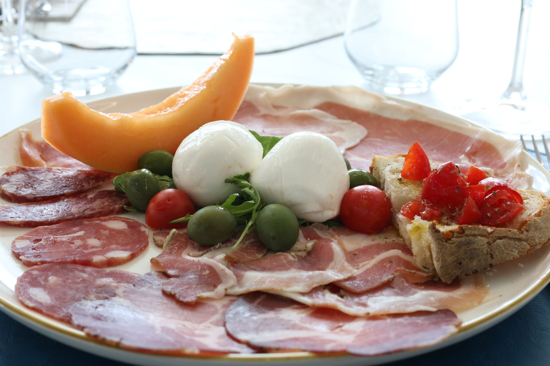 Piatto di antipasti italiani: salumi, mozzarella, olive, melone e bruschetta al pomodoro.