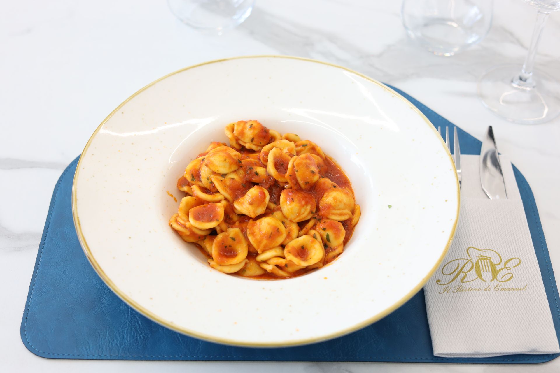 Sala da pranzo del ristorante con tavoli in marmo bianco, sedie e tovagliette color verde acqua. I tavoli sono apparecchiati per i clienti.