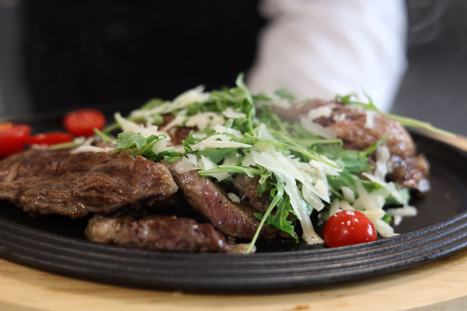 Fette di bistecca condite con rucola, formaggio a scaglie e pomodorini su una piastra di ghisa.