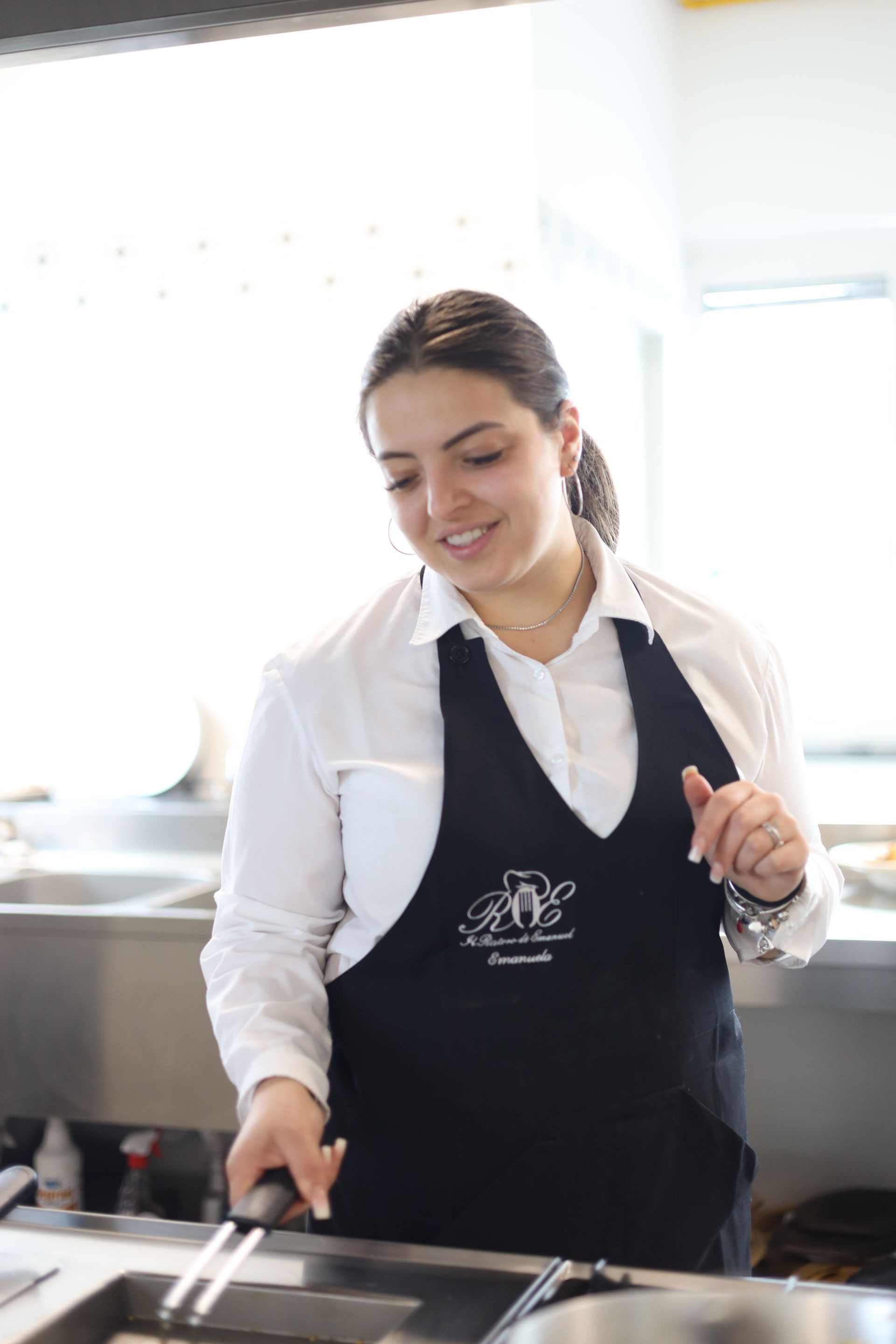 Una donna che indossa un grembiule nero e una camicia bianca sorride mentre cucina in cucina.