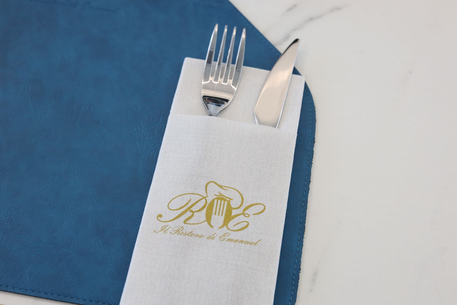 Sala da pranzo del ristorante con tavoli con piano in marmo, bicchieri e posate. Sedie color verde acqua e opere d'arte decorano le pareti bianche.