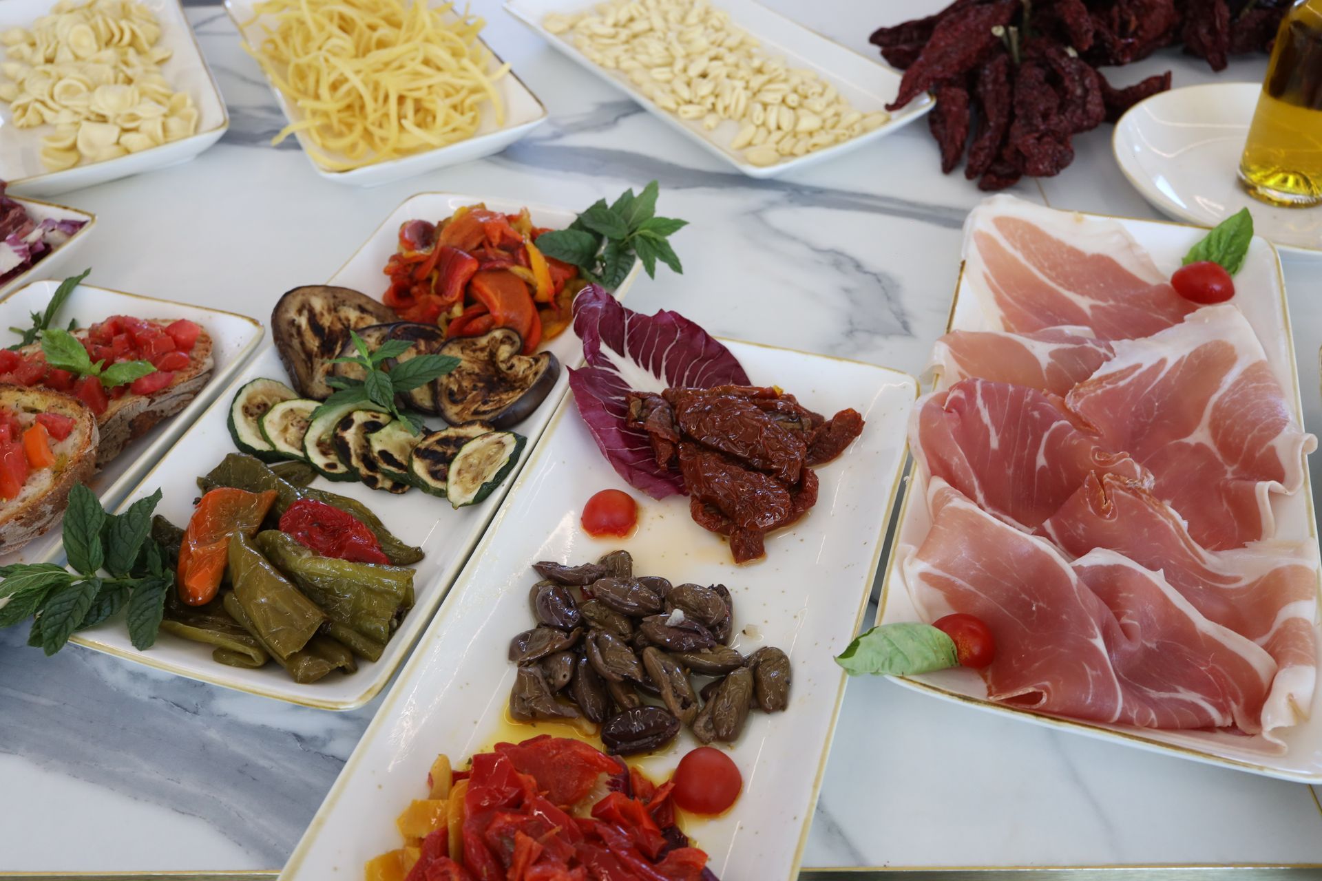 Patio esterno con tavoli e sedie con vista sul paesaggio montuoso, sotto un cielo azzurro e con mulini a vento in lontananza.