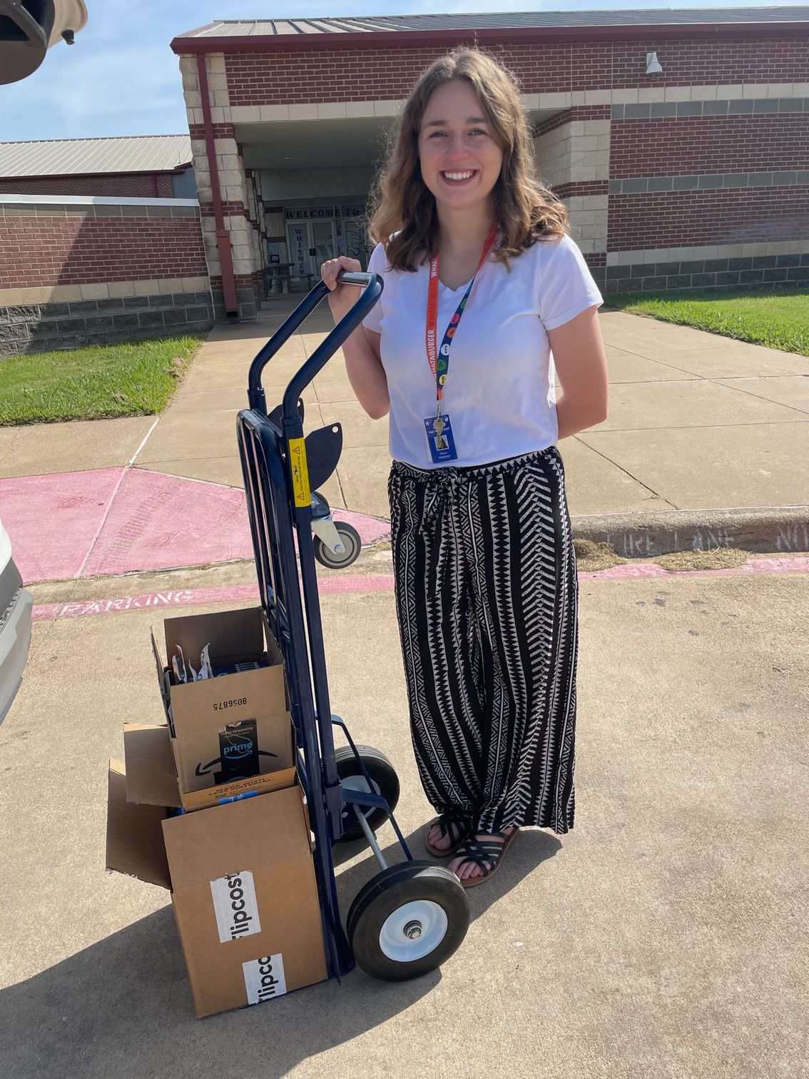 A woman is standing next to a hand truck full of boxes.