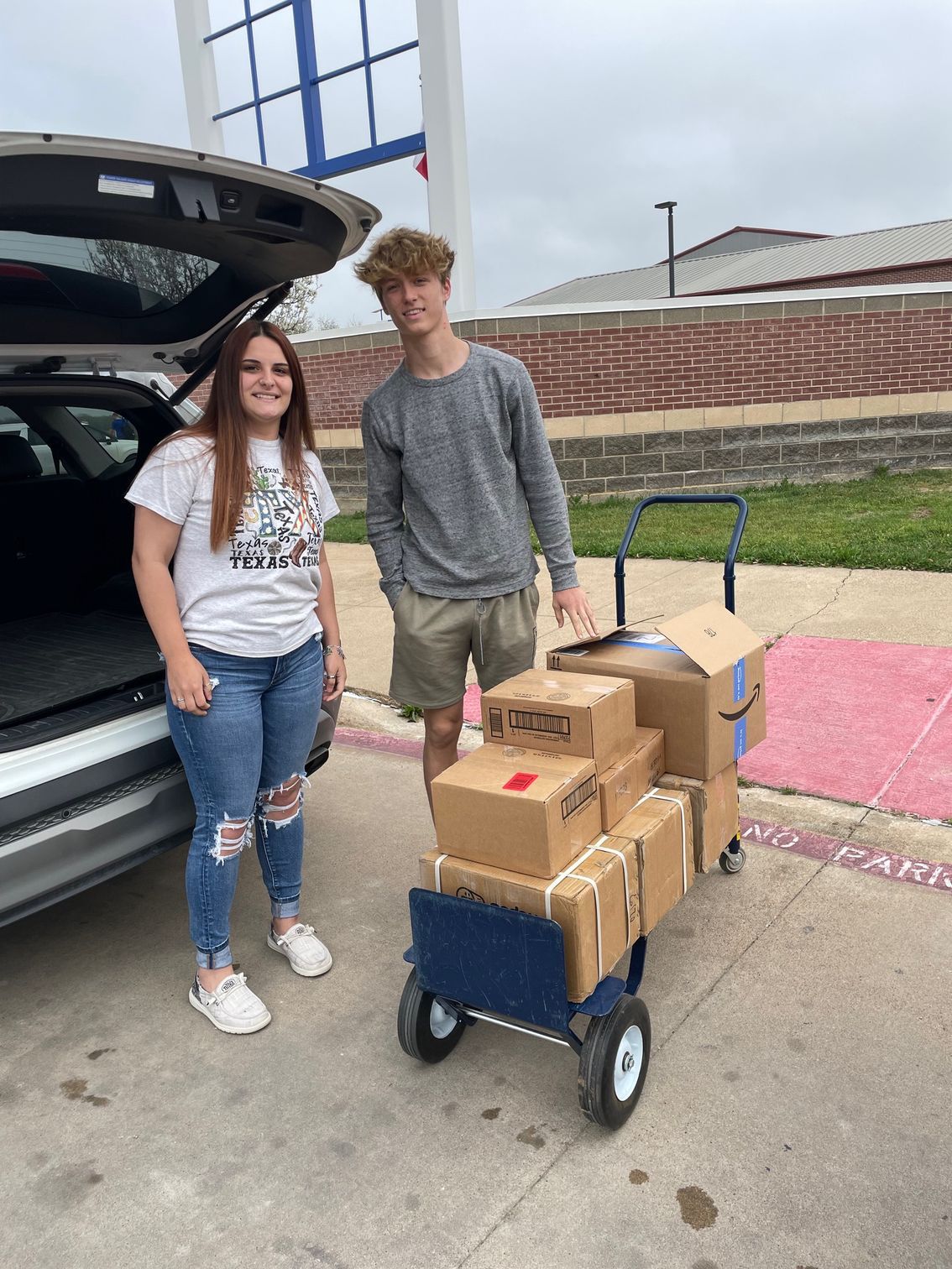 A man and a woman are standing next to a cart filled with boxes.