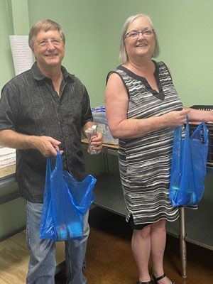 A man and a woman are standing next to each other holding blue bags.