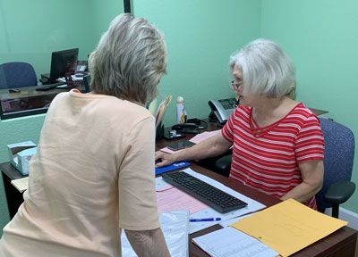 Two women are sitting at a desk talking to each other.