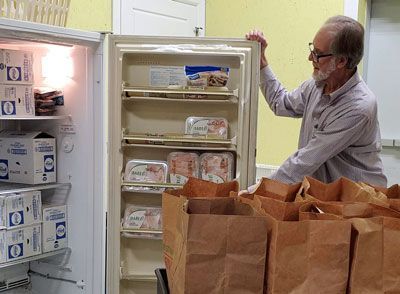 A man is standing in front of a refrigerator filled with food.