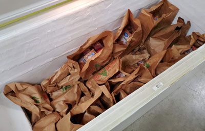 A freezer filled with brown paper bags filled with food.