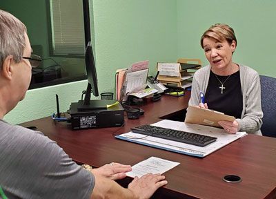 A woman is sitting at a desk talking to a man.