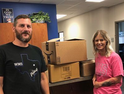 A man and a woman are standing next to each other in front of a pile of cardboard boxes.