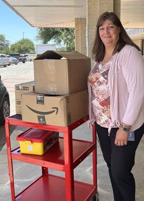 A woman is standing next to a red cart with boxes on it.