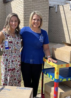 Two women are standing next to each other in front of a brick building.