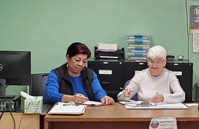 Two women are sitting at a desk in front of a computer.