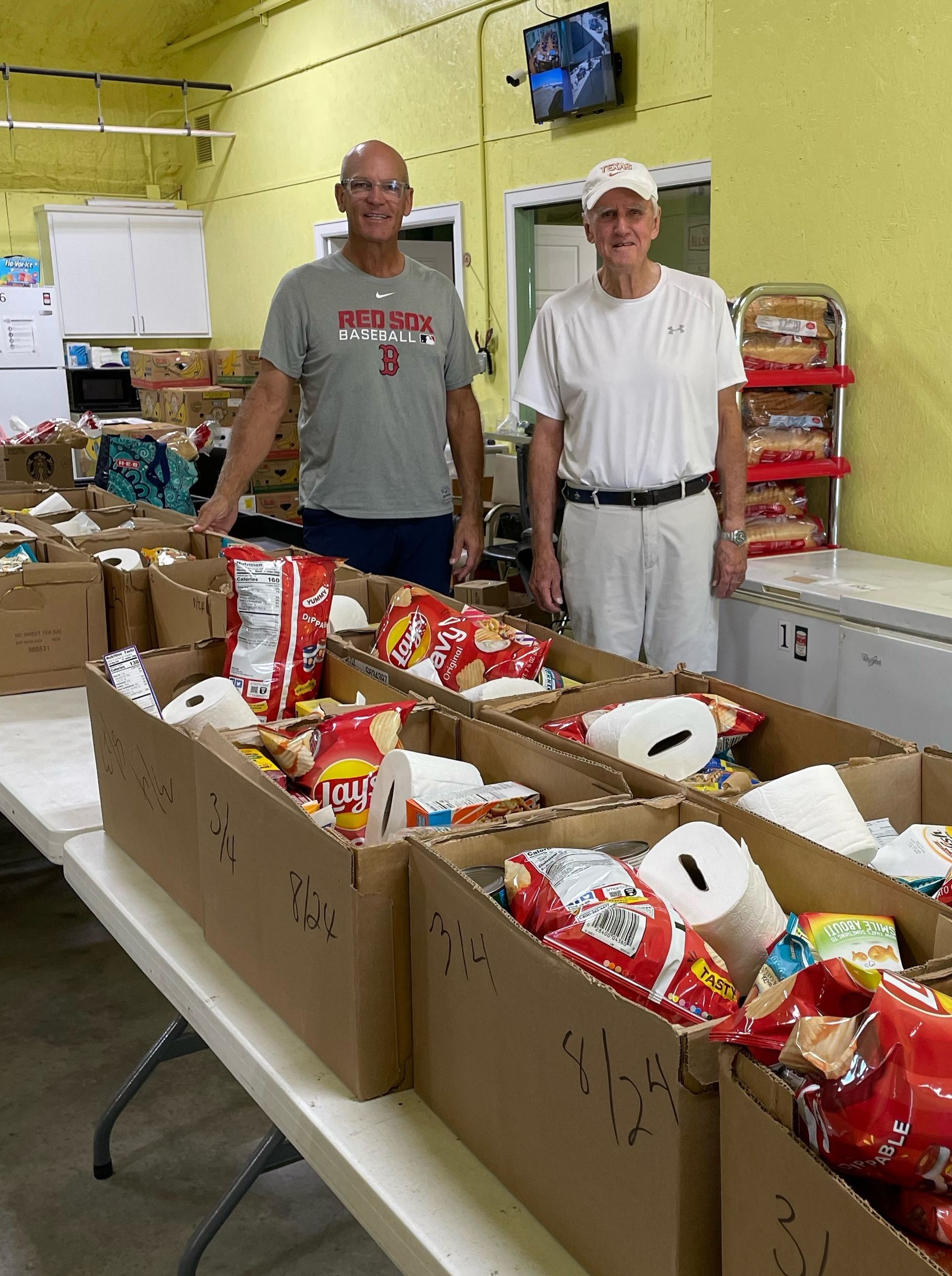 Two men are standing in front of a table filled with boxes of food.