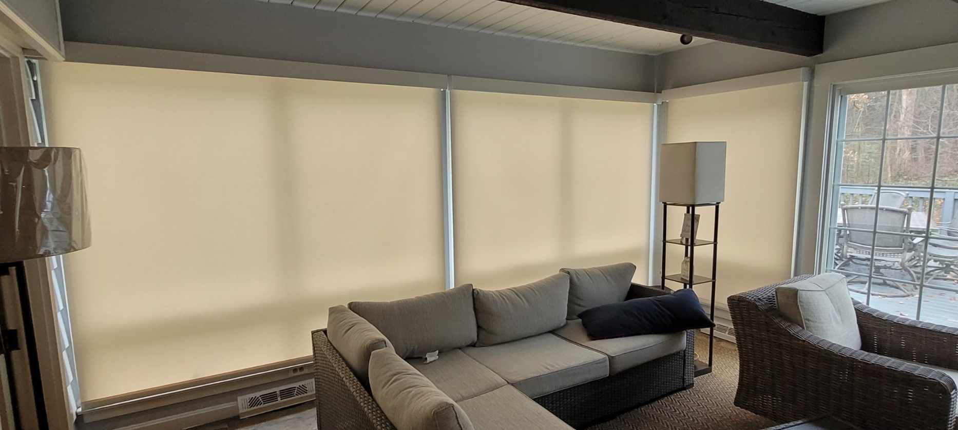 Sunroom with neutral-colored roller shades, sectional sofa, and wicker chair.