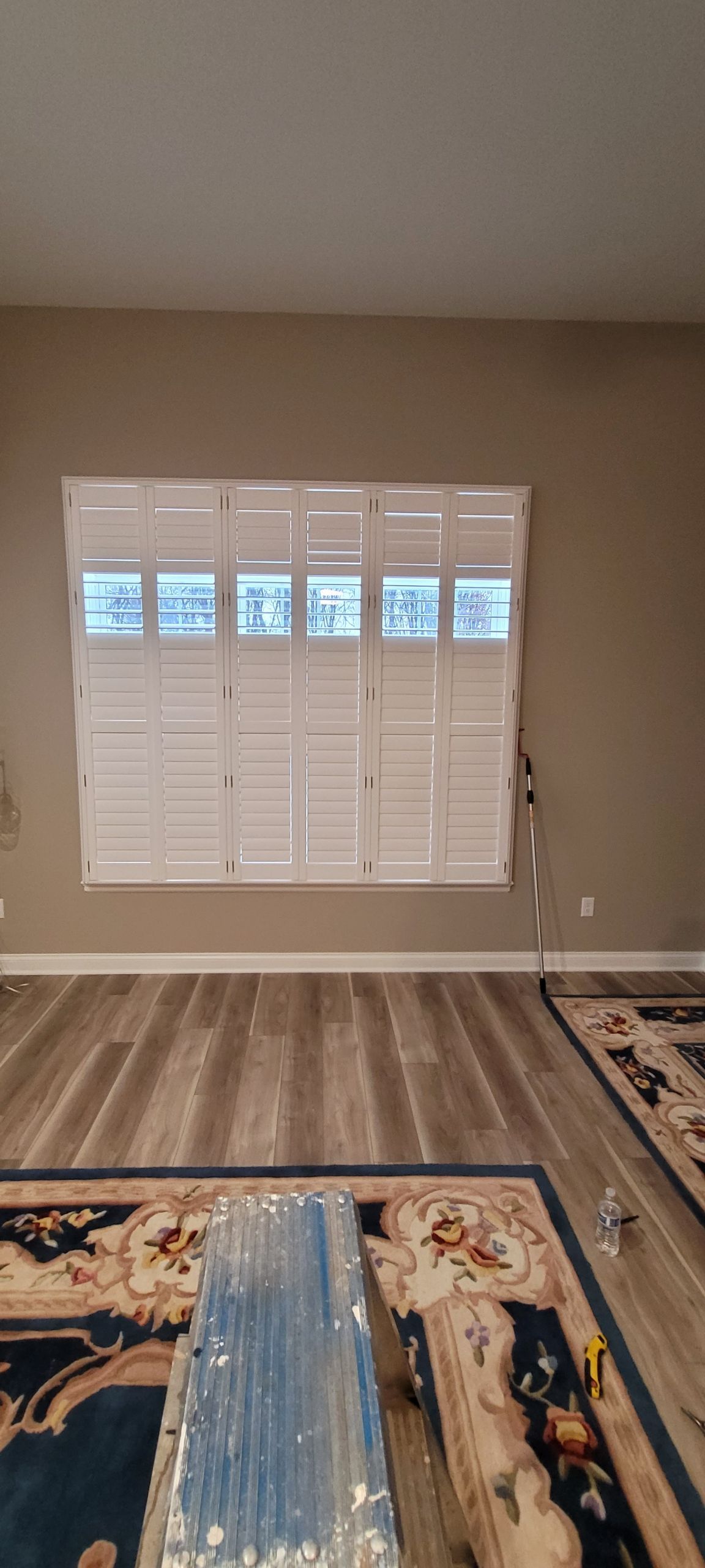 Interior with window and white shutters.  Gray wall, wood-look floor, and patterned rugs.