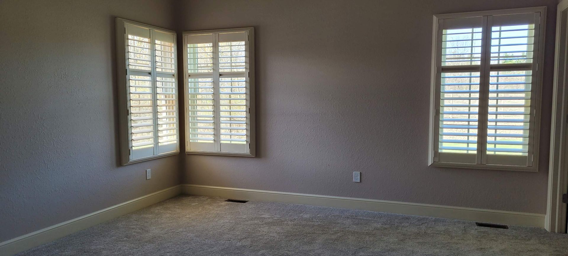 Empty room with two windows and white shutters; mauve walls, light carpet.
