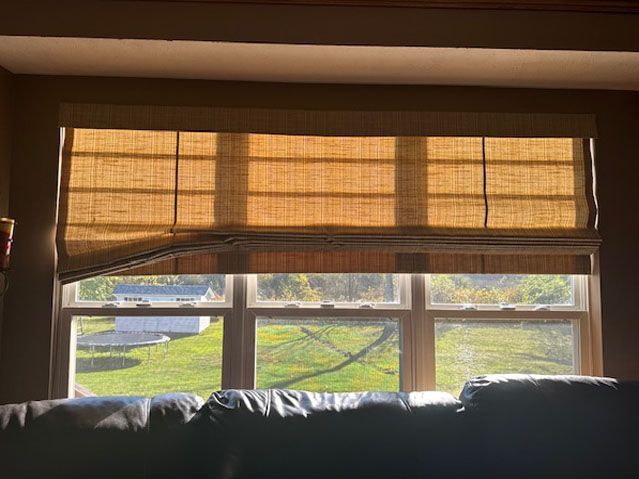 Window with bamboo shades partially lowered, showing an outdoor view of grass and buildings.