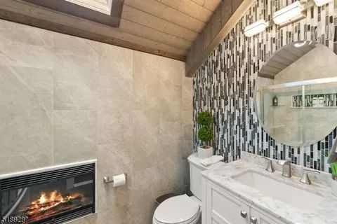 A bathroom with a toilet , sink , mirror and fireplace.
