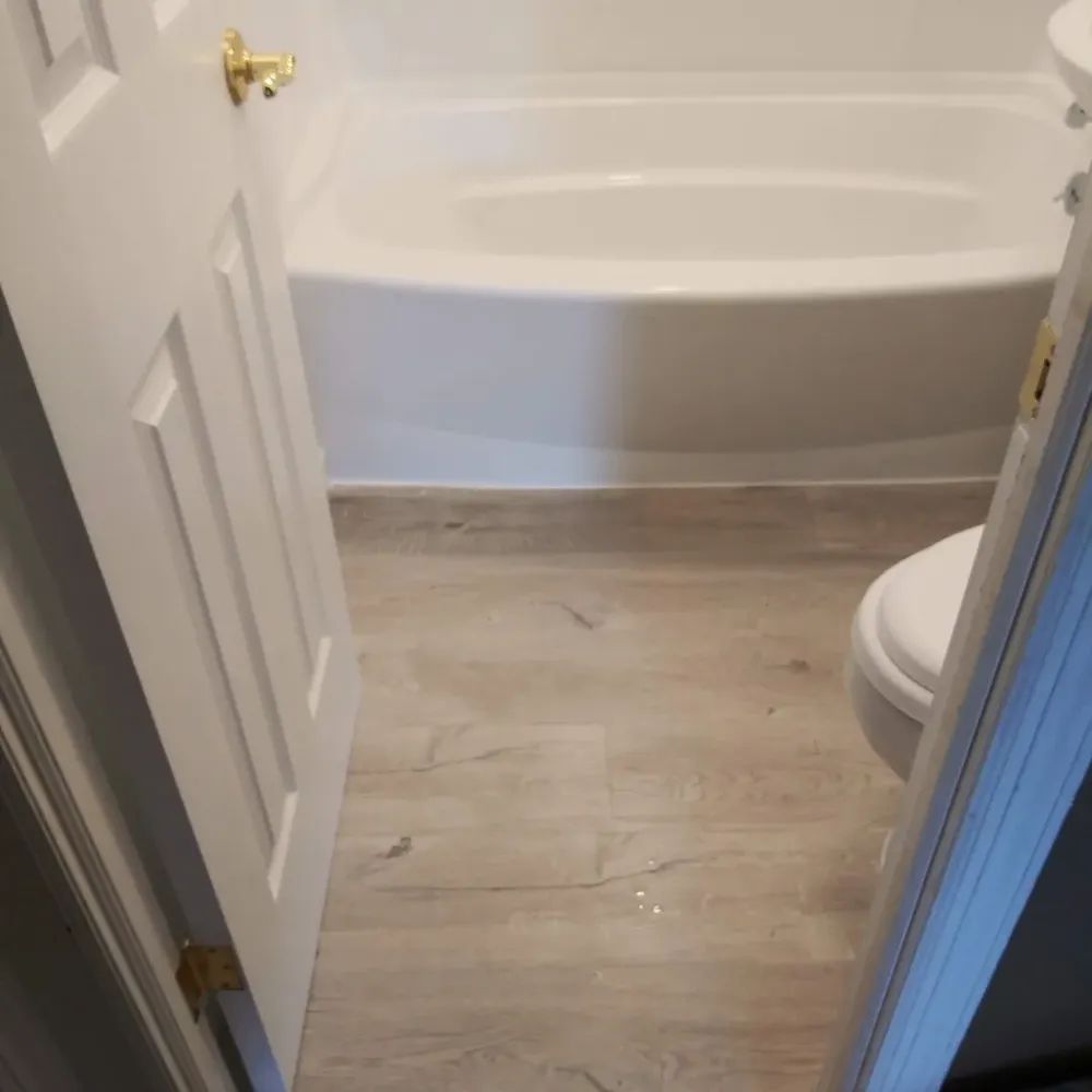A bathroom with a tub, toilet, and wooden floor