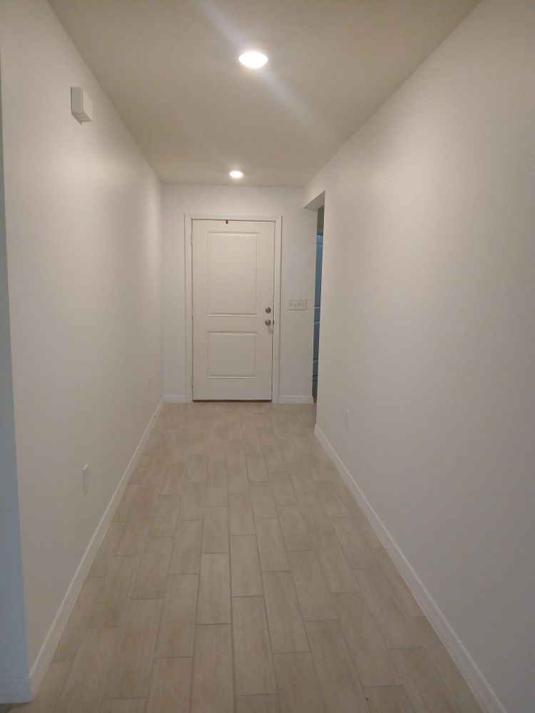 A long hallway with white walls and tile floors leading to a door