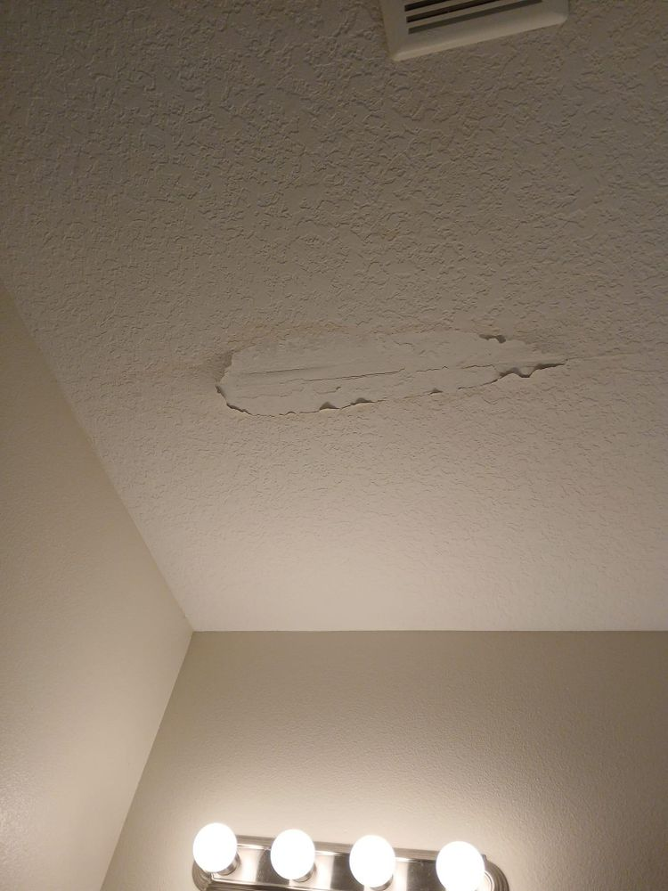 A bathroom with a ceiling that has peeling paint and a light fixture.