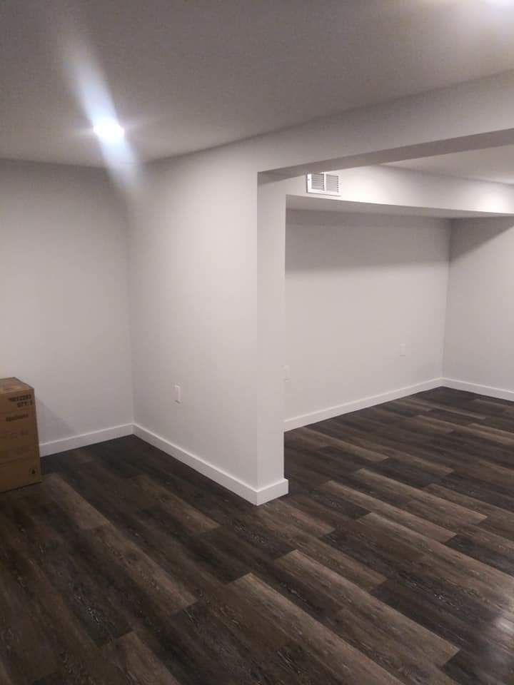 An empty basement with hardwood floors and white walls