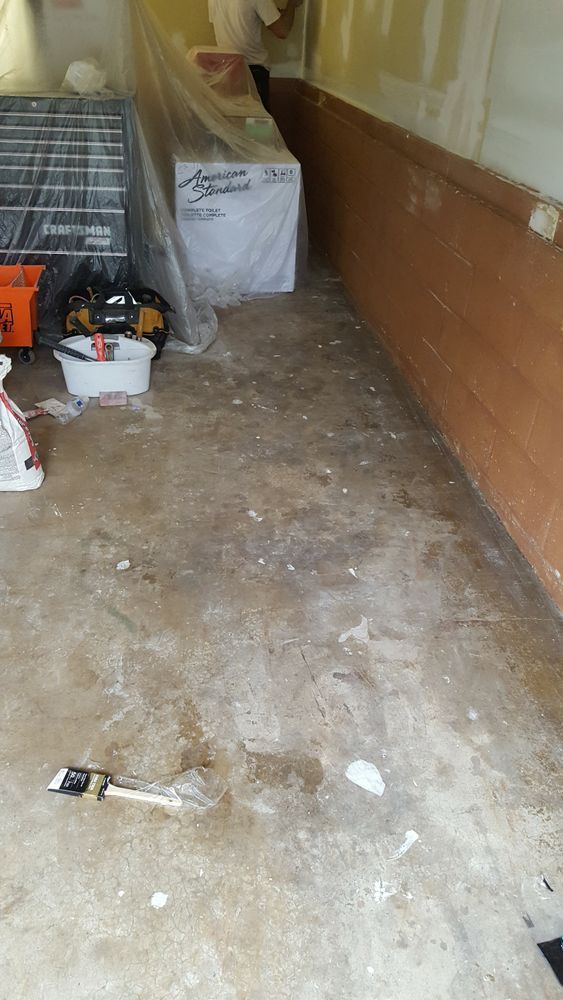 A dirty floor in a garage with a refrigerator in the background