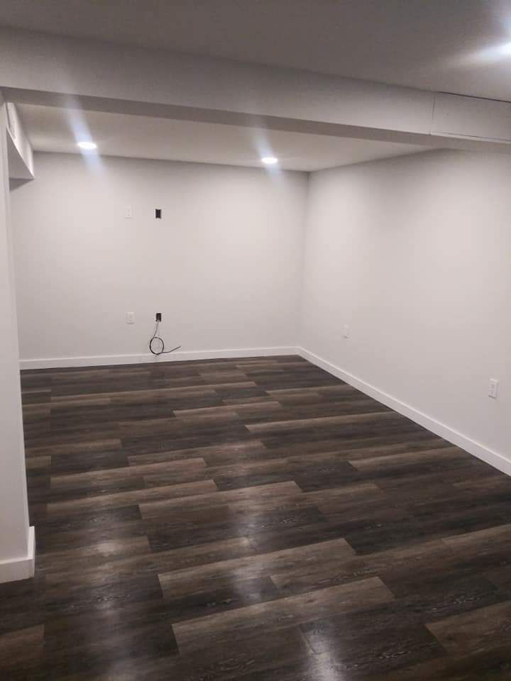 An empty basement with hardwood floors and white walls