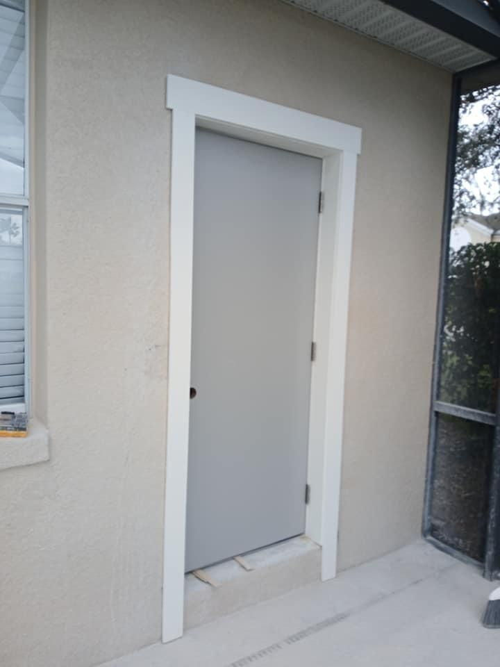 A gray door with a white trim is on the side of a house