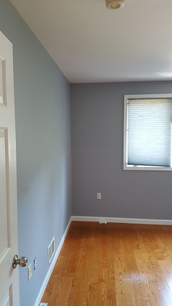 A bedroom with gray walls and hardwood floors and a window